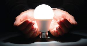 A man with his hands out resting underneath a lightbulb