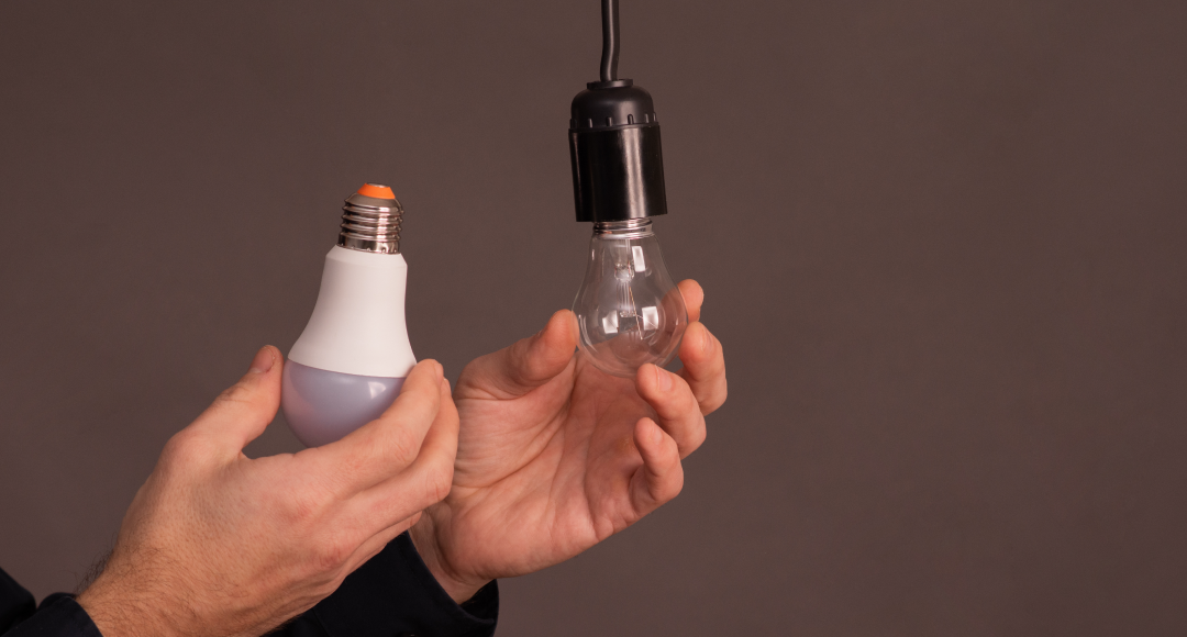 Man holding an LED bulb on one hand and a regular bulb on the other.